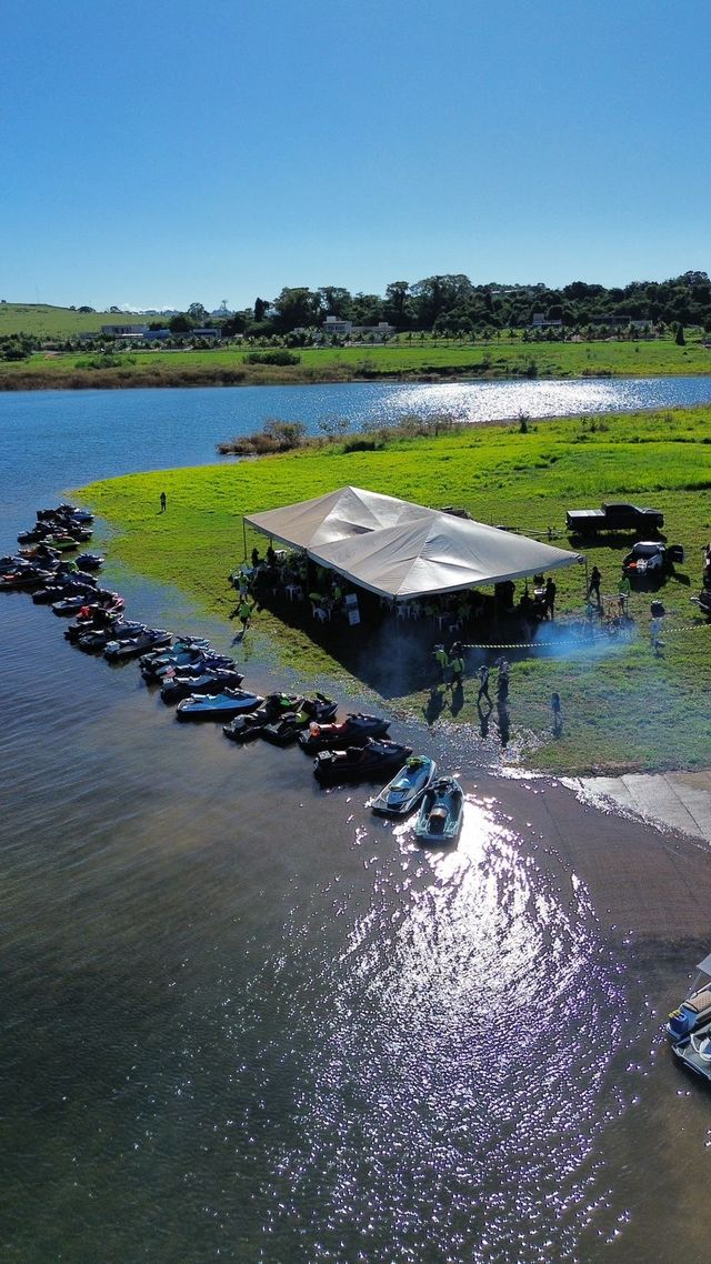 Tenda do evento e fila de jet skis na margem, vista de cima