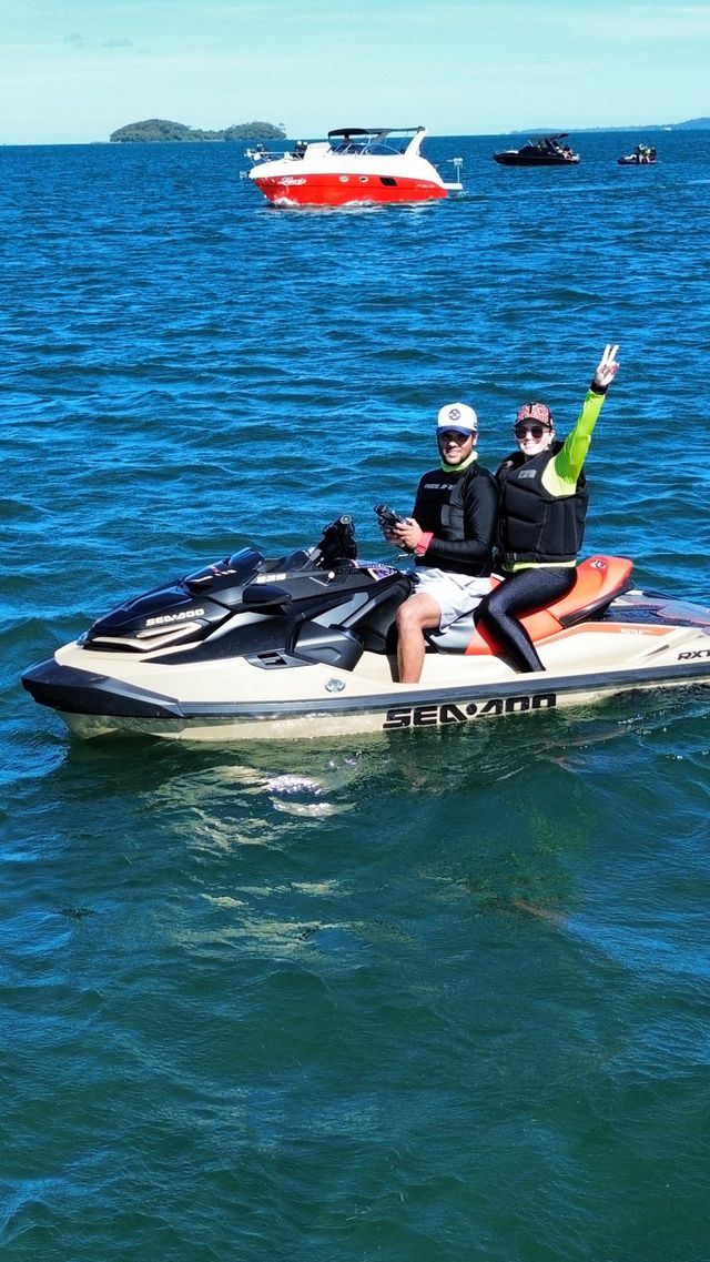 Casal pilotando jet ski com lanchas ao fundo